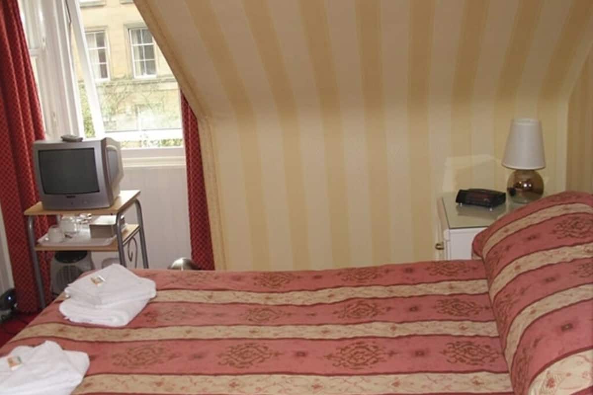 A hotel room with a bed, a television on a small table, a lamp, and a window with curtains.