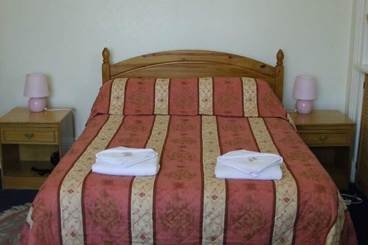 A neatly made bed with a striped bedspread and two folded towels on it. There are two bedside tables with lamps on either side of the bed.