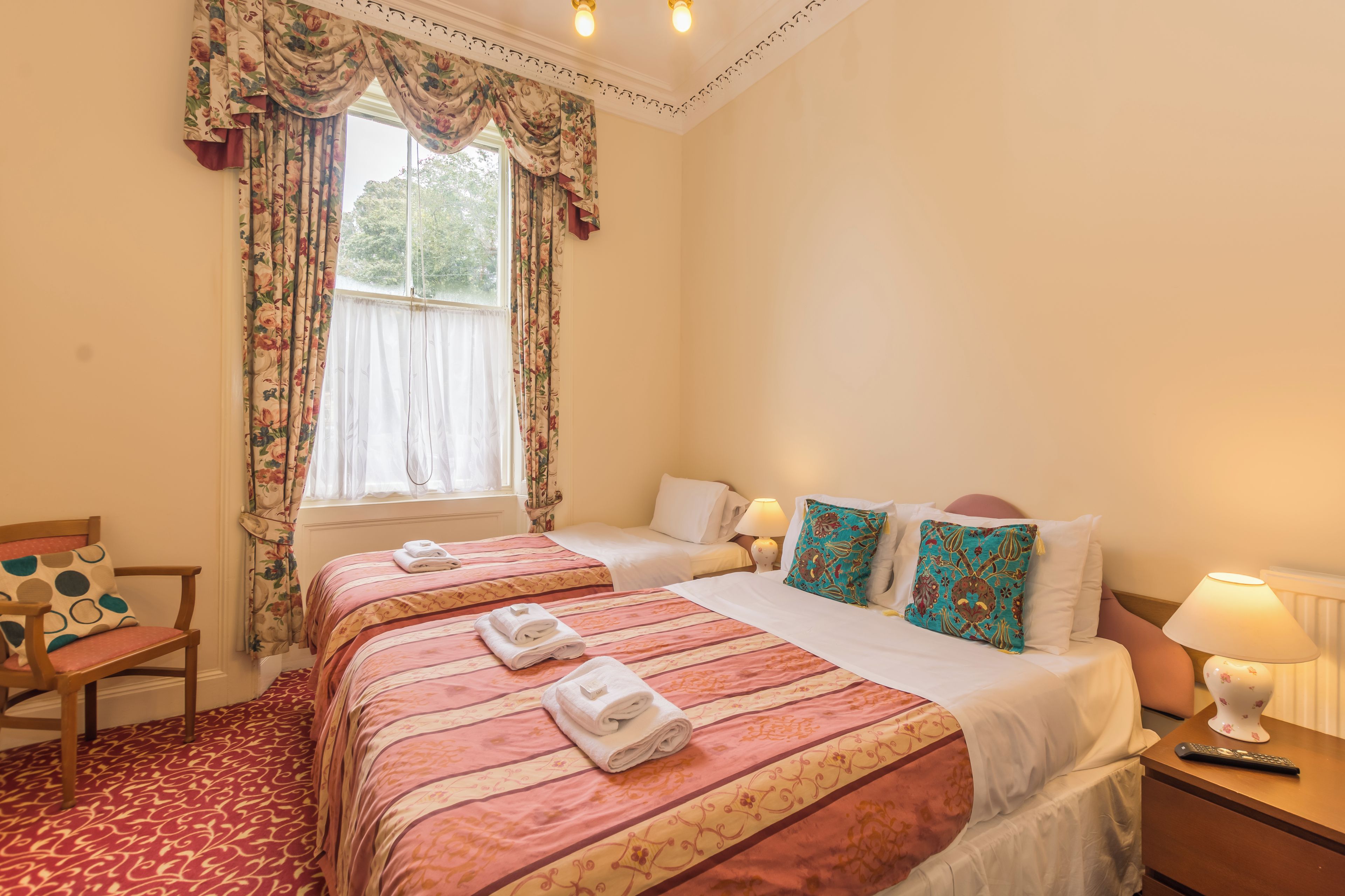 A hotel room with two beds, a chair, a window with curtains, and a lamp on the nightstand.
