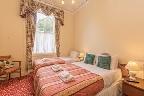 A hotel room with two beds, a chair, a window with curtains, and a lamp on the nightstand. - Menzies Guest House (Edinburgh)