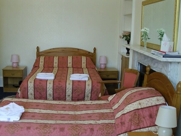 A neatly made bed with a patterned bedspread, two bedside tables with lamps, a chair, and a fireplace with a mirror above it. - Menzies Guest House (Edinburgh)