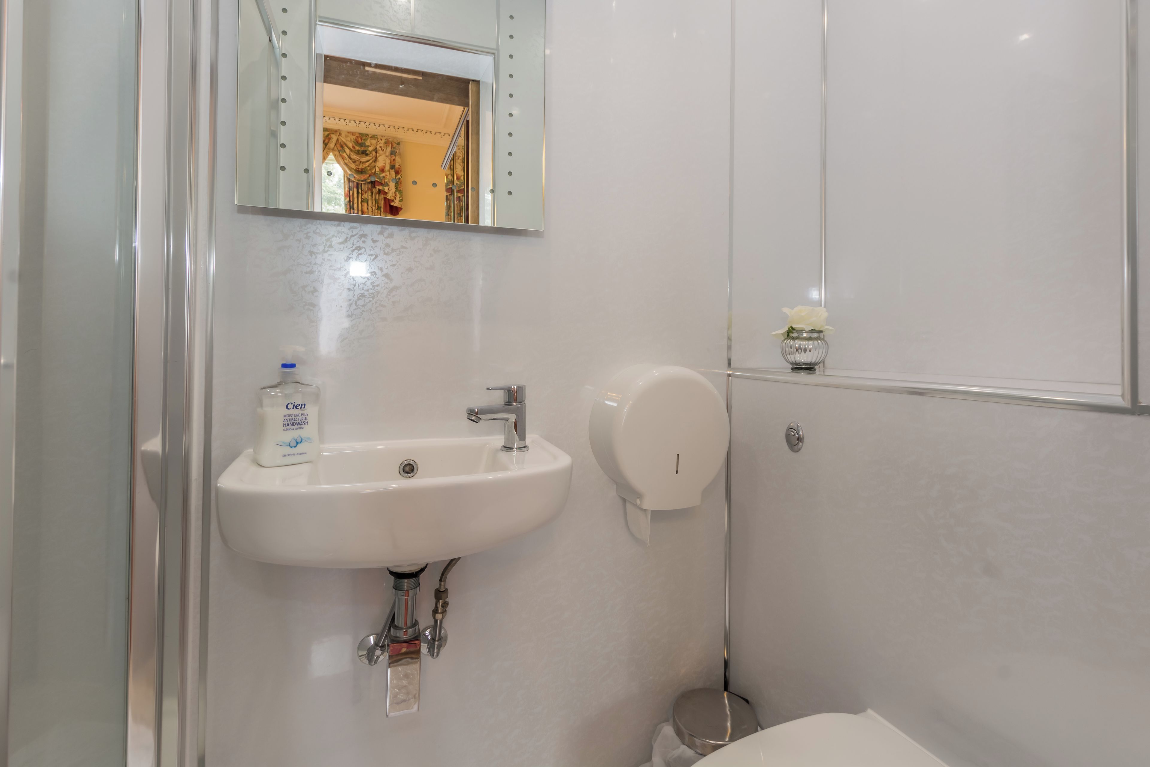 Casa de banho com lavatório branco, espelho e secador de mãos.