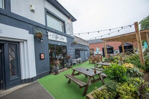A hotel exterior with a coffee shop, outdoor seating, and a garden area.