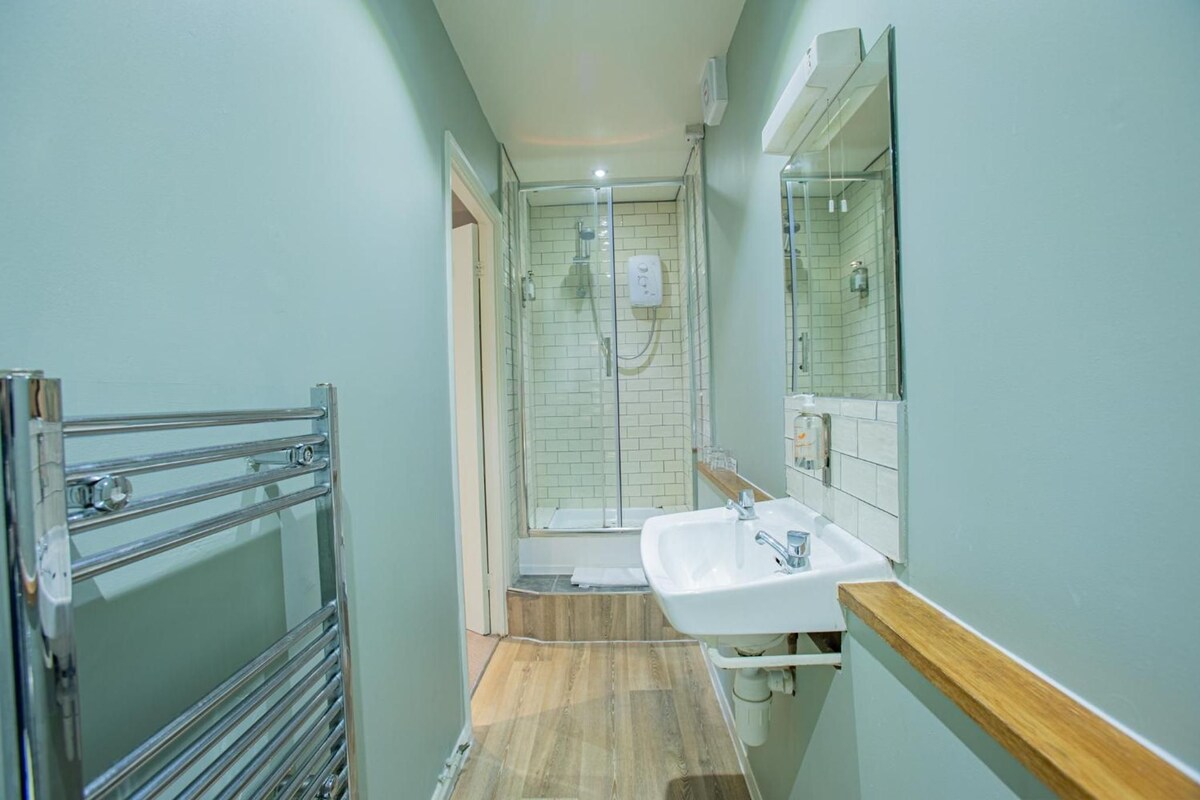 A narrow bathroom with a shower, a sink, and a mirror.