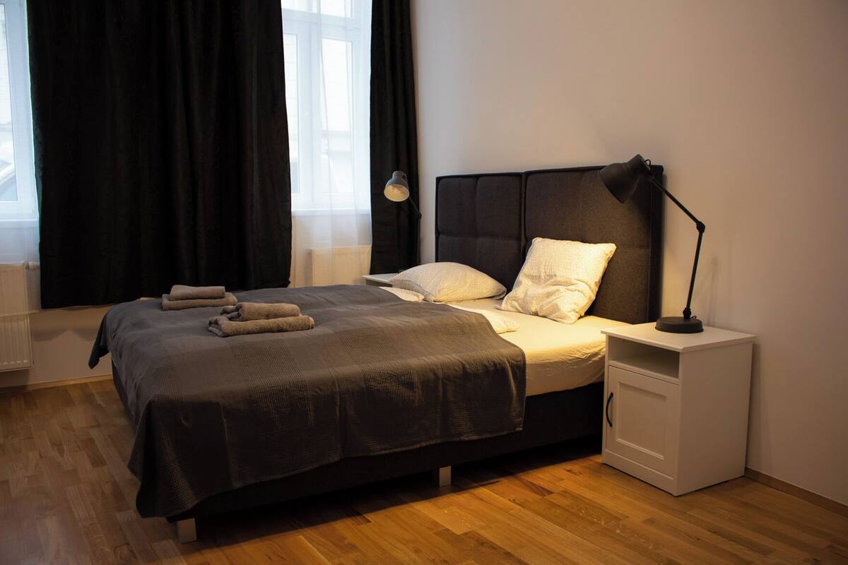 A neatly made bed with a dark headboard, a bedside lamp, and a small white nightstand.