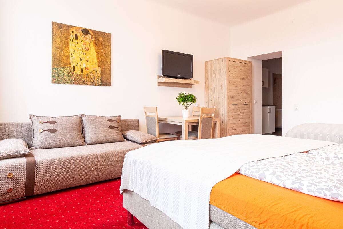 A hotel room with a bed, a sofa, a desk, a chair, a television, and a painting on the wall.