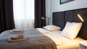 A neatly made bed with a checkered bedspread, two pillows, and two folded towels. - Hotel & Apartments Klimt (Vienna)