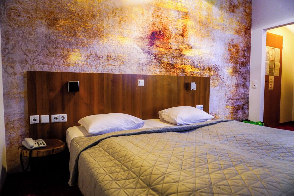 A hotel room with a wooden headboard, two beds with white linens, a bedside table with a phone, and a wall with a textured pattern.