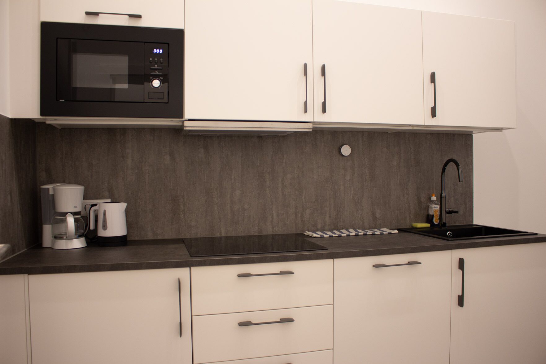 Una cocina moderna con microondas integrado, cafetera y lavamanos.