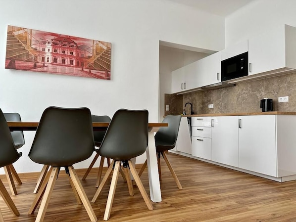 Eine moderne Küche mit weißen Schränken, einer schwarzen Mikrowelle und einem Holzespeisetisch mit Stühlen.