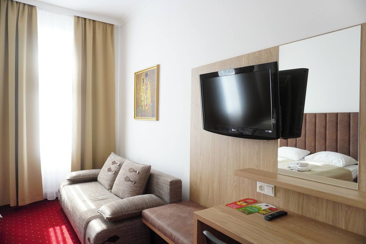 A hotel room with a sofa, a TV mounted on the wall, a mirror, and a small table with a remote control.