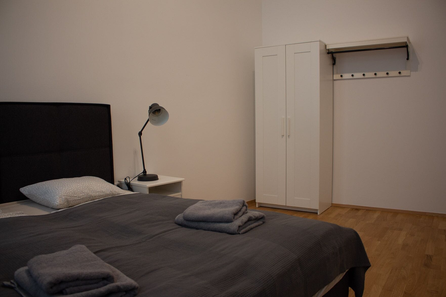 A bedroom with a bed, a bedside lamp, a wardrobe, and a wall-mounted shelf.