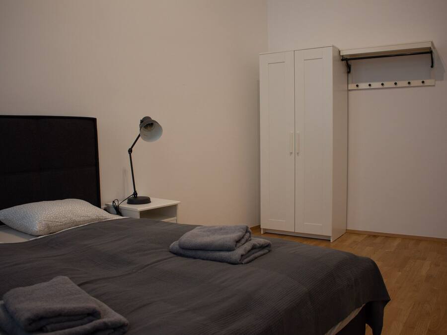 A bedroom with a bed, a bedside lamp, a wardrobe, and a wall-mounted shelf.