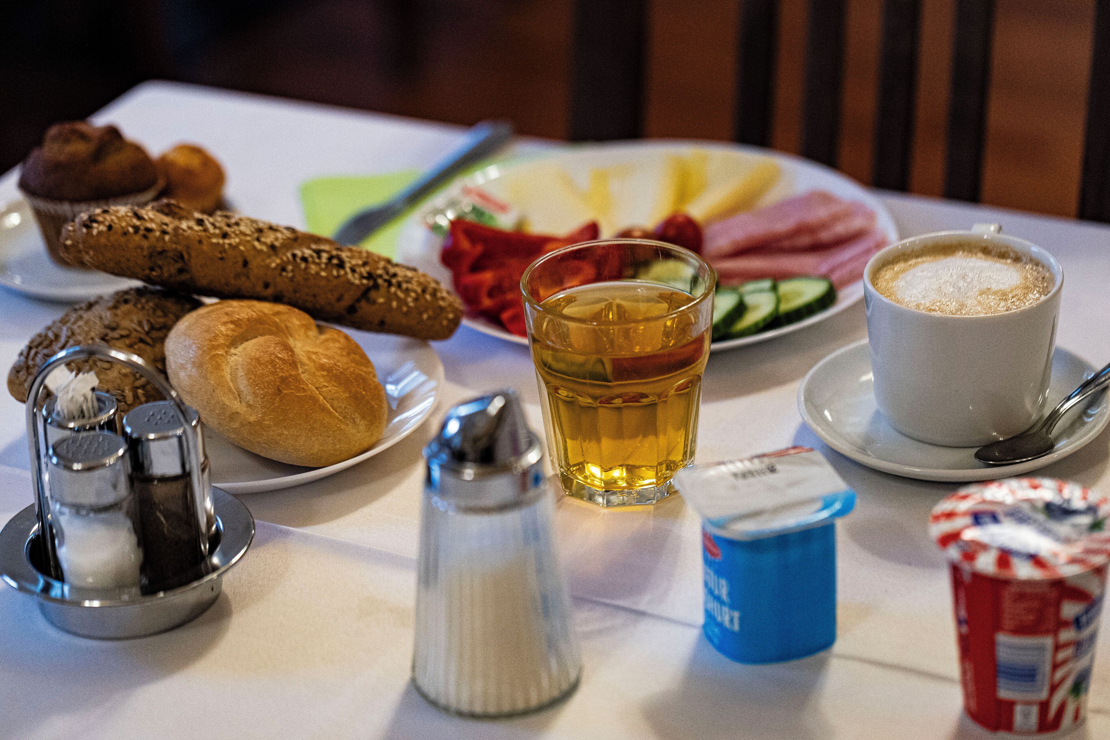 A table with food items, a glass of tea, a cup of coffee, and condiments.