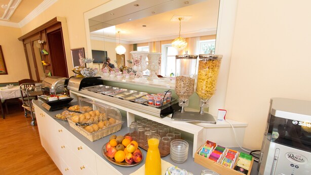 A buffet with various food items, a juice dispenser, and a coffee machine. - Hotel & Apartments Klimt (Vienna)