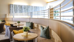 A modern lounge area with round tables, cushioned seating, and potted plants.