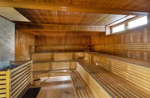 A sauna with wooden benches and a stone wall. - JUFA Hotel Bruck (Bruck an der Mur)