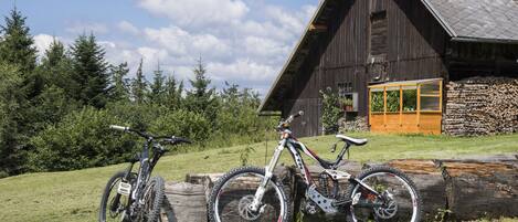 A rustic wooden building with a sloped roof, a large wooden log, and two bicycles parked in front.