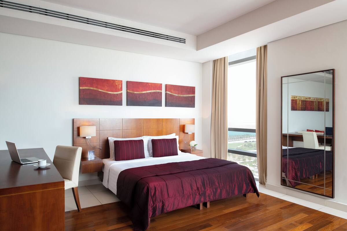 Habitación de hotel moderna con una cama grande, un escritorio con una computadora portátil y vistas al exterior.