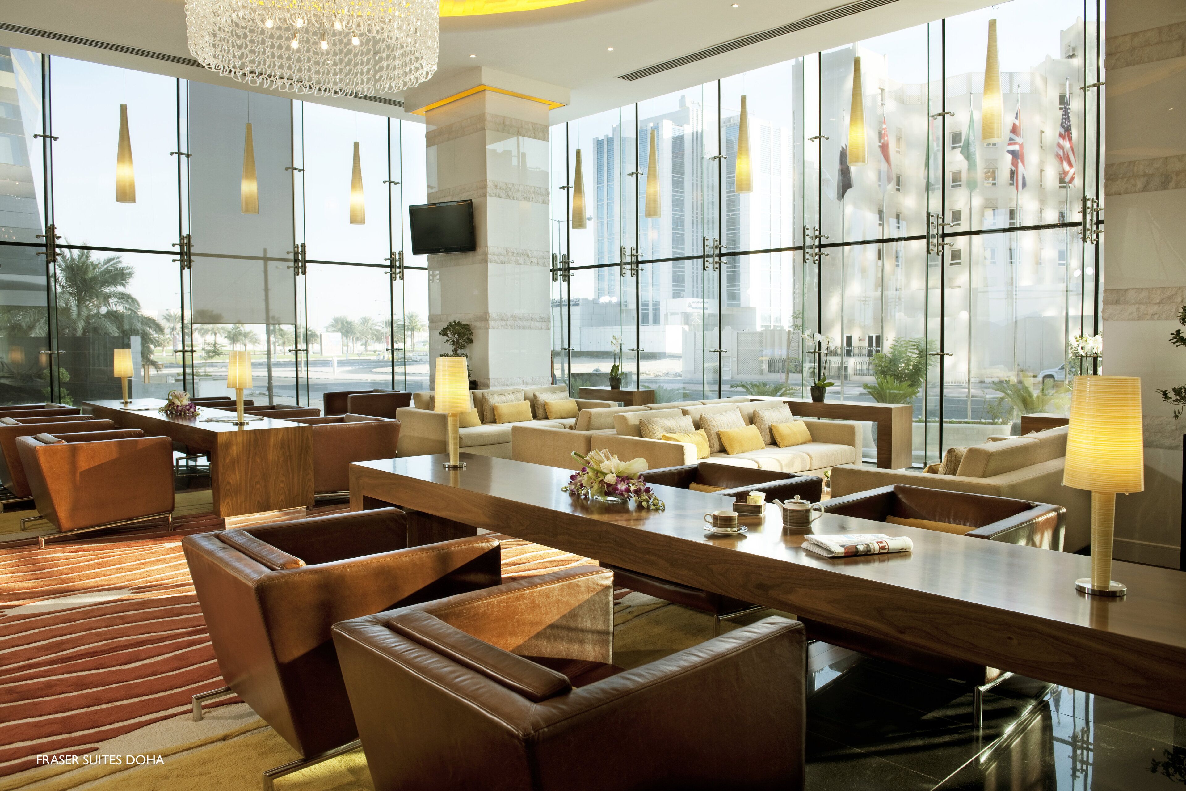 A modern hotel lobby with leather seating, a wooden reception desk, and large windows offering city views.