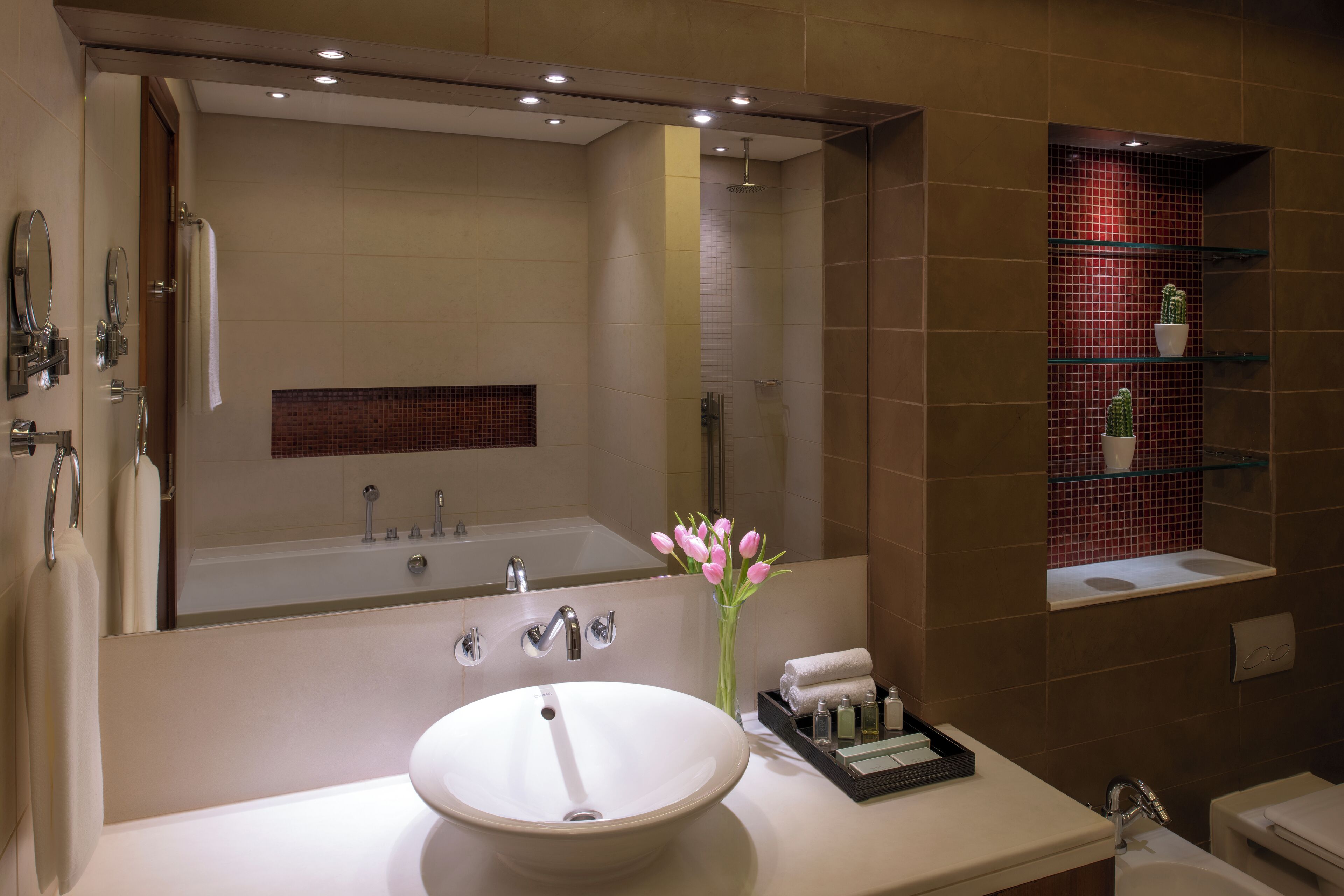 Un baño moderno con un espejo grande, un lavabo, una bañera y un estante con artículos de aseo.