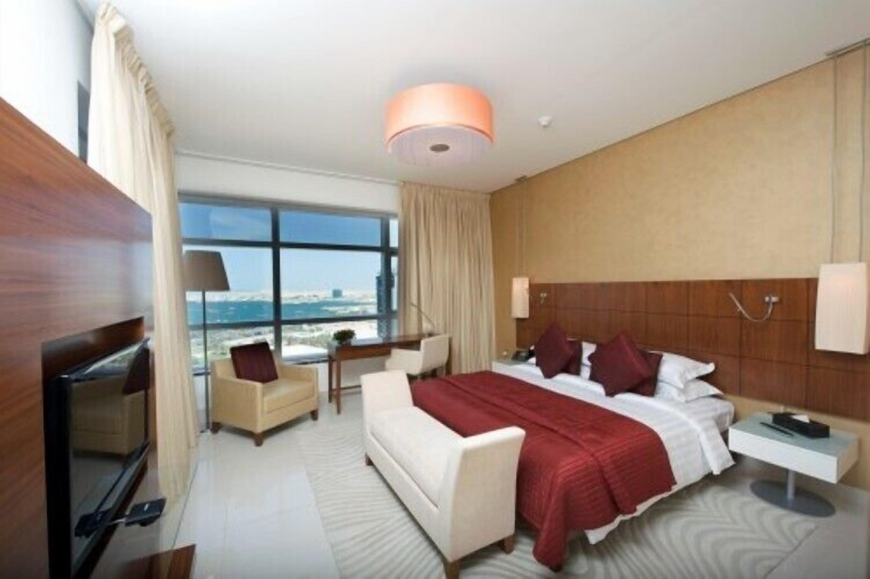 Una habitación de hotel moderna con una cama grande, un escritorio, una silla, un televisor y vistas a la ciudad.
