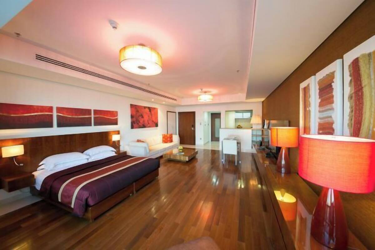 Una habitación de hotel con una cama grande, mesitas de noche, un sofá, un rincón de comedor y obras de arte en las paredes.