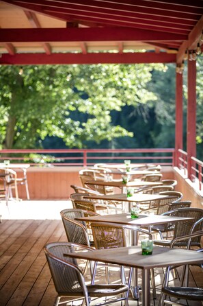 Guests can dine al fresco under a shaded deck with comfortable seating and a beautiful natural backdrop.