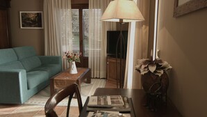 A living room with a green sofa, a coffee table with a vase of flowers, a lamp, and a television. - HOTEL FINCA EL VENTÓS (Sant Aniol de Finestres)