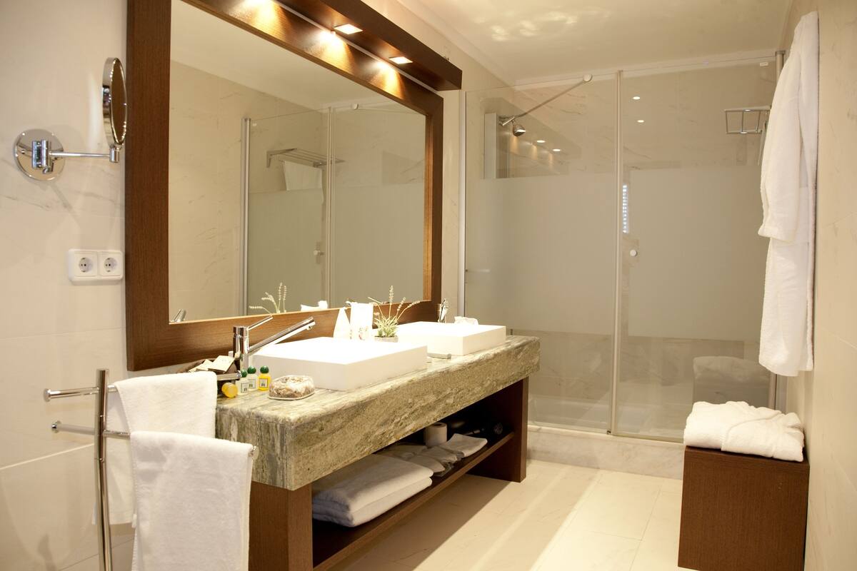 A modern bathroom with a large mirror, two sinks, a shower, and a towel rack.