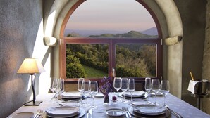 A table set for six with wine glasses, plates, and cutlery, a candle, and a bottle of champagne, with a scenic view through an arched window. - HOTEL FINCA EL VENTÓS (Sant Aniol de Finestres)