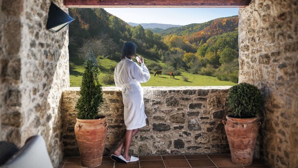 A stone-walled balcony with terracotta pots, a wooden ceiling, and a view of a green valley. - HOTEL FINCA EL VENTÓS (Sant Aniol de Finestres)