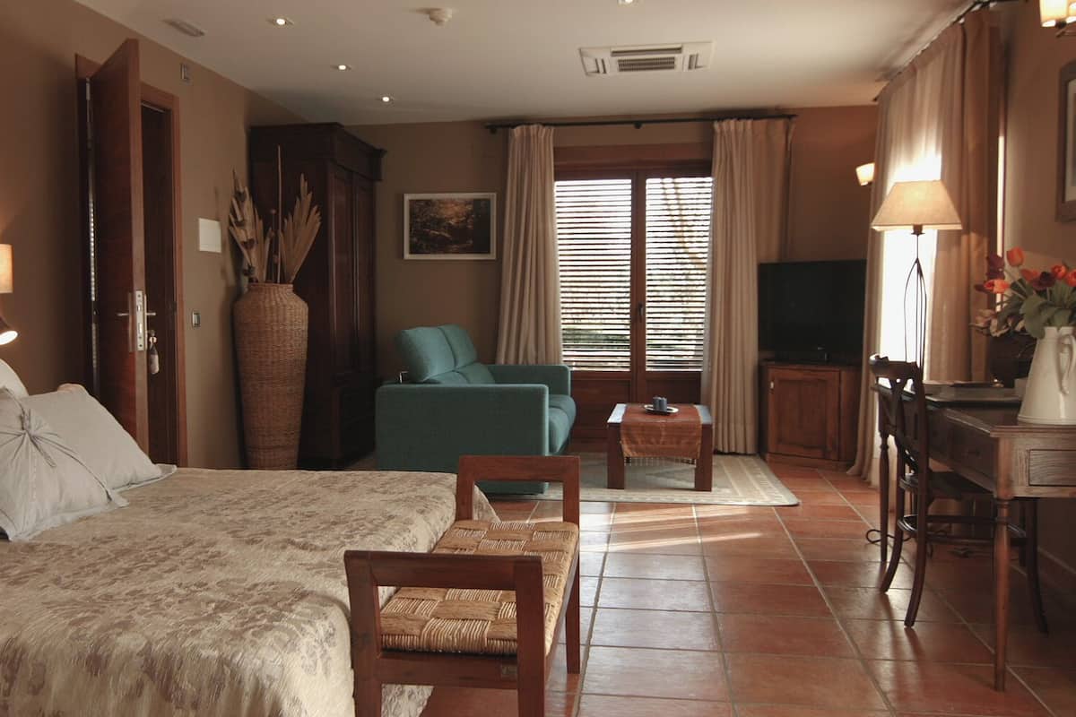 A bedroom with a large bed, a green armchair, a small table, and a TV.