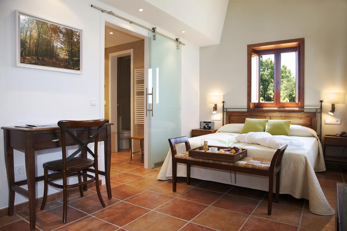 A bedroom with a bed, bedside table, lamp, and a desk with a chair.