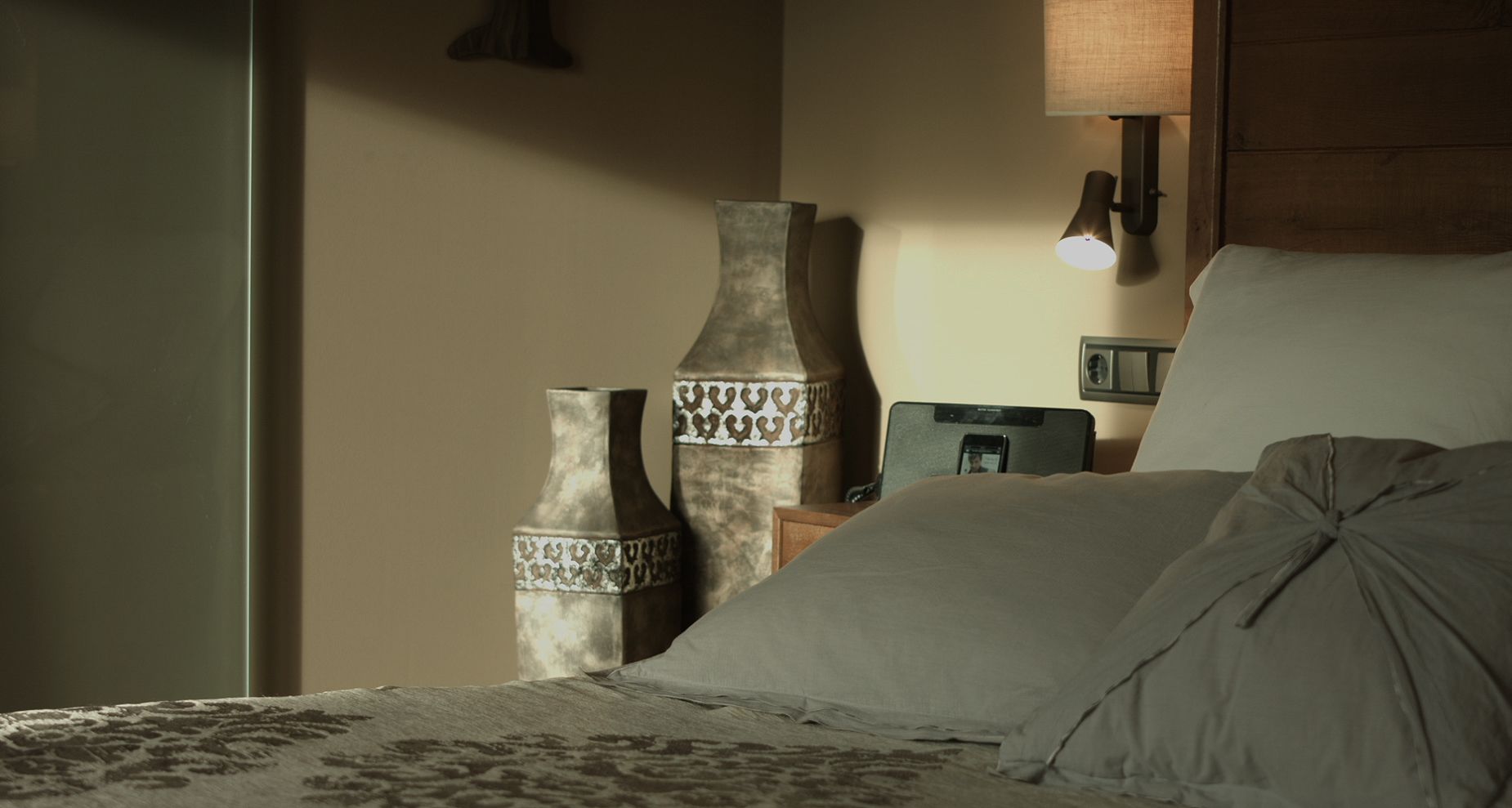 A bedroom with a bed, two decorative vases, a nightstand, a lamp, and a mirror.