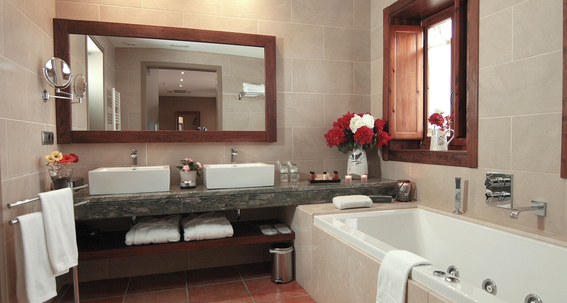 A modern bathroom with two sinks, a large bathtub, a vanity with a mirror, and a window.