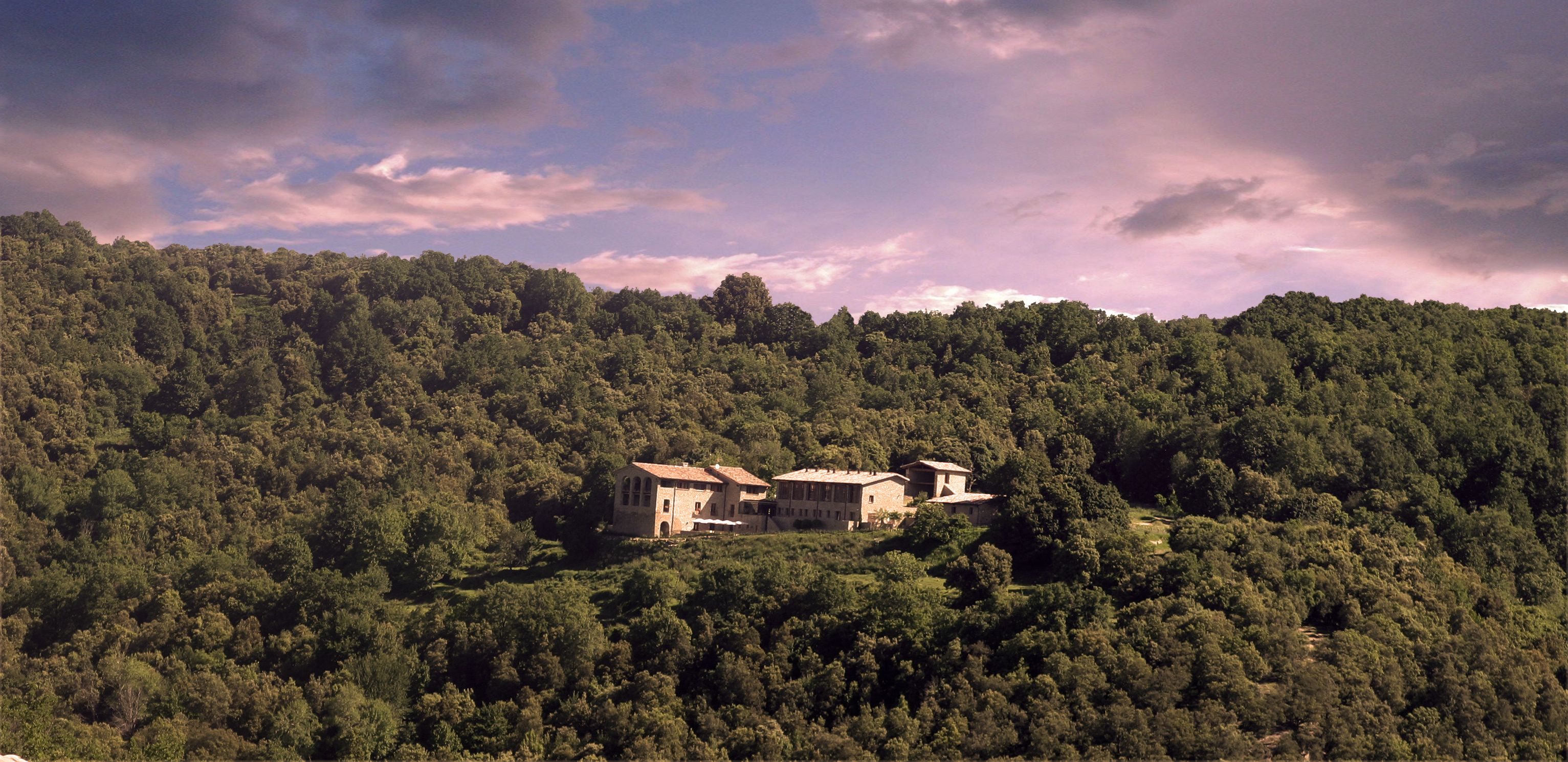 A large, rustic building with a stone facade, surrounded by dense forest on a hillside.