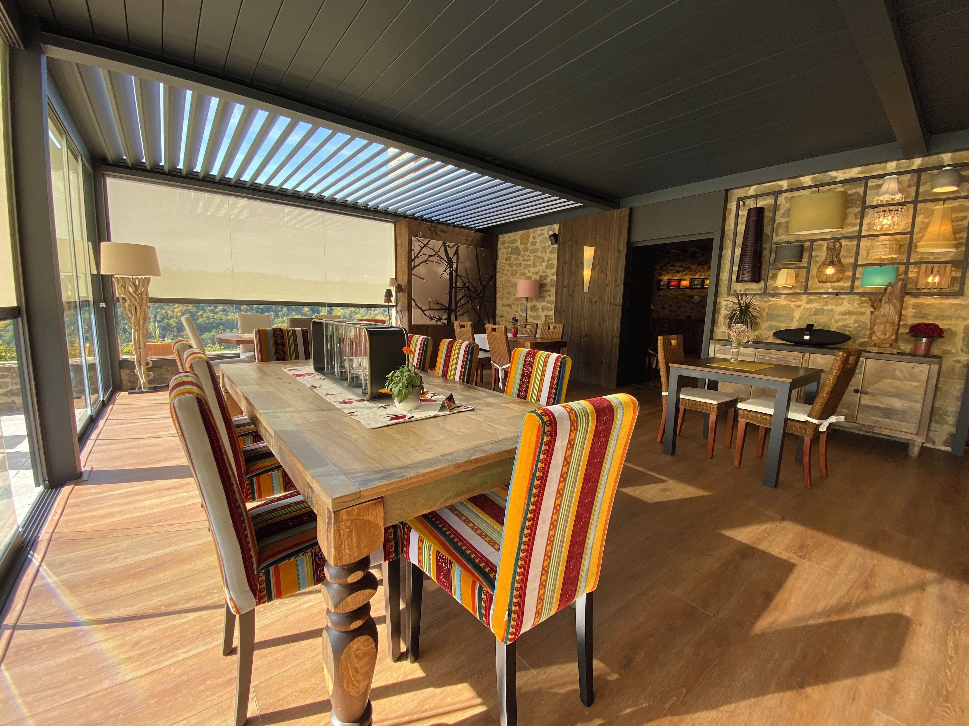A spacious dining area with a long wooden table, striped chairs, and a stone wall backdrop.