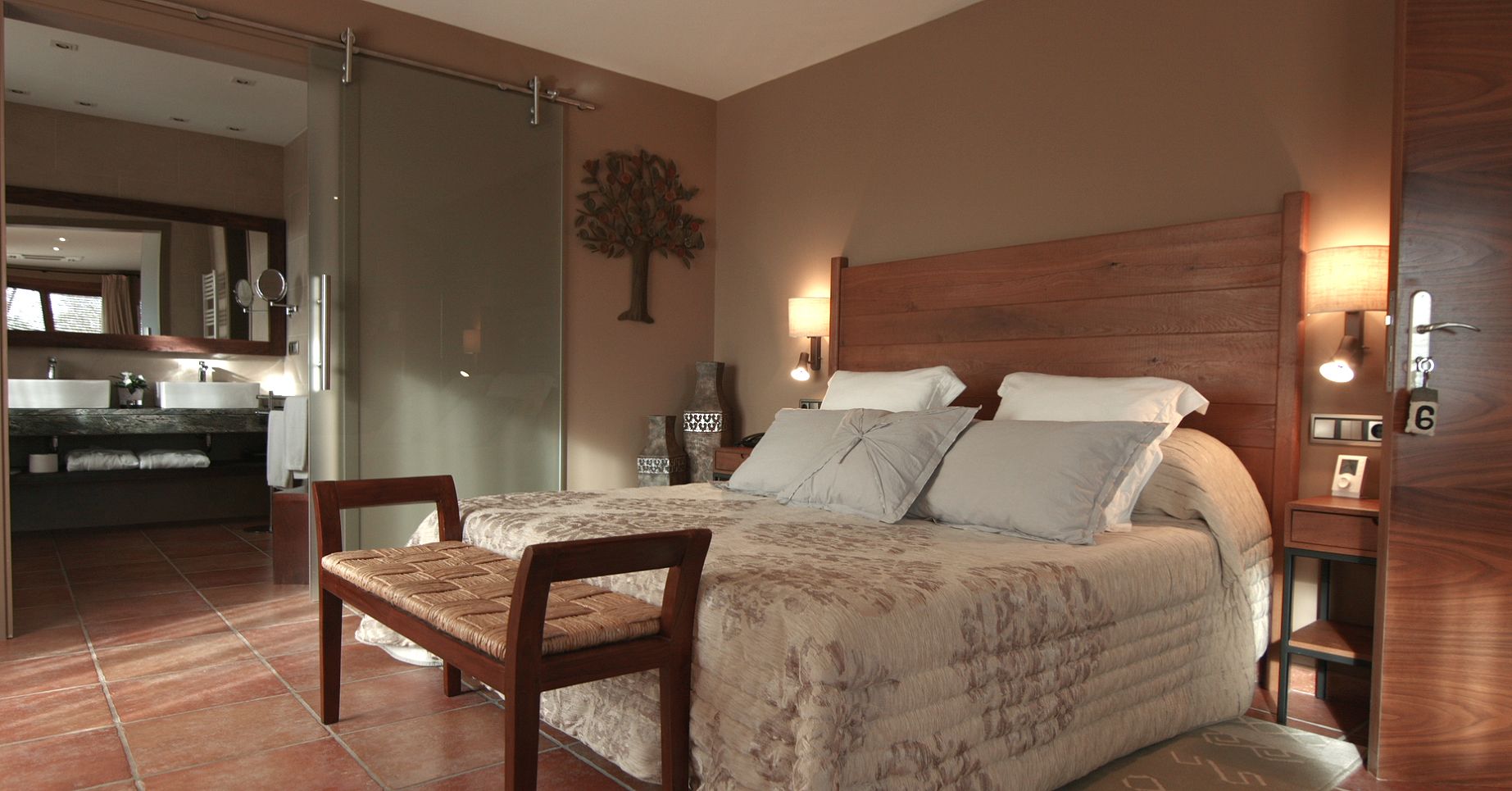 Habitación de hotel con dos camas, un área de descanso, un baño con espejo y un cabecero de madera.