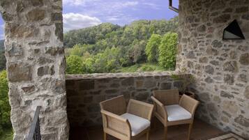 Un balcon en pierre avec deux fauteuils en osier et une vue sur une colline boisée.