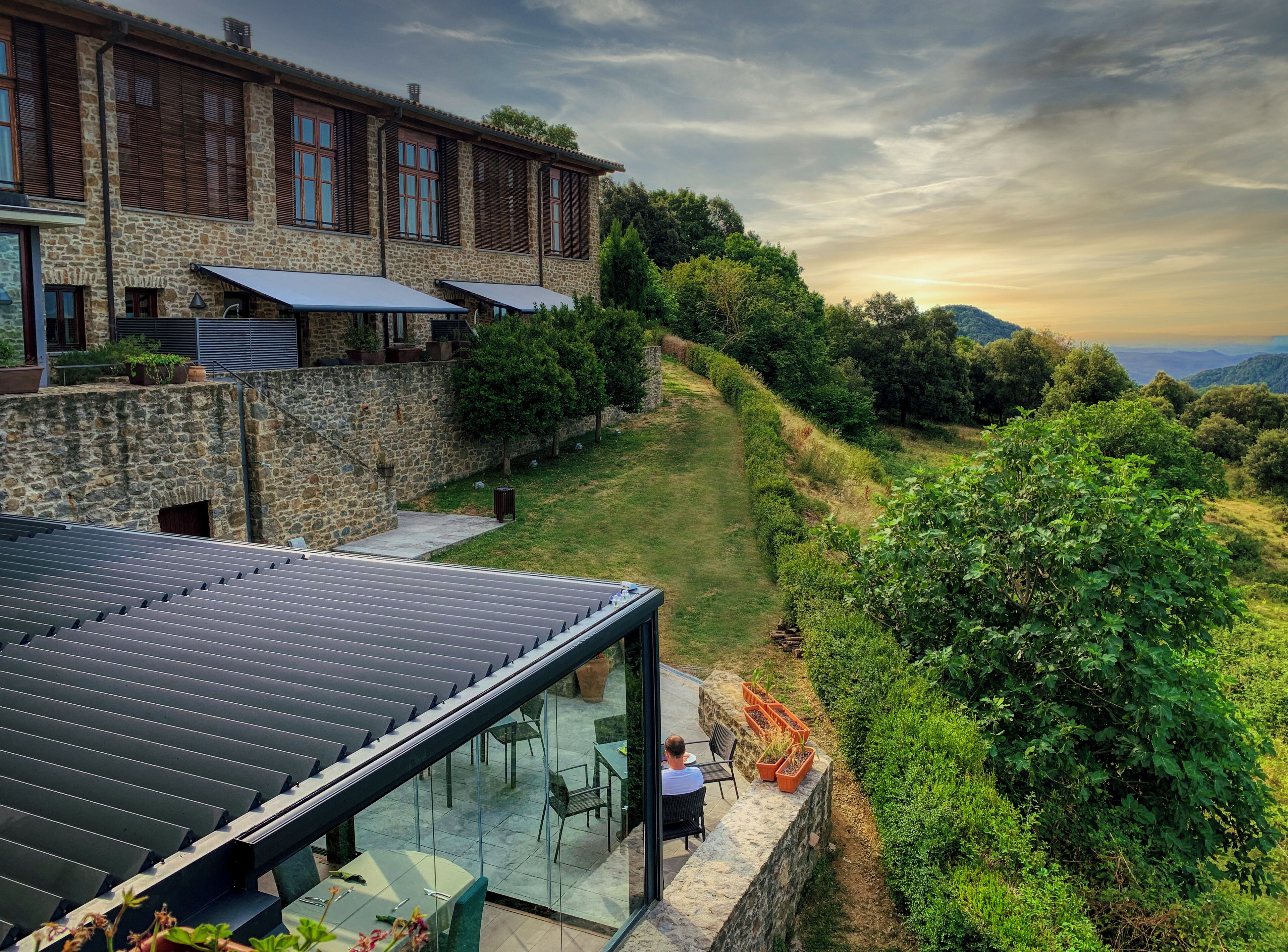 A stone building with a terrace, outdoor seating, and a view of the surrounding landscape.