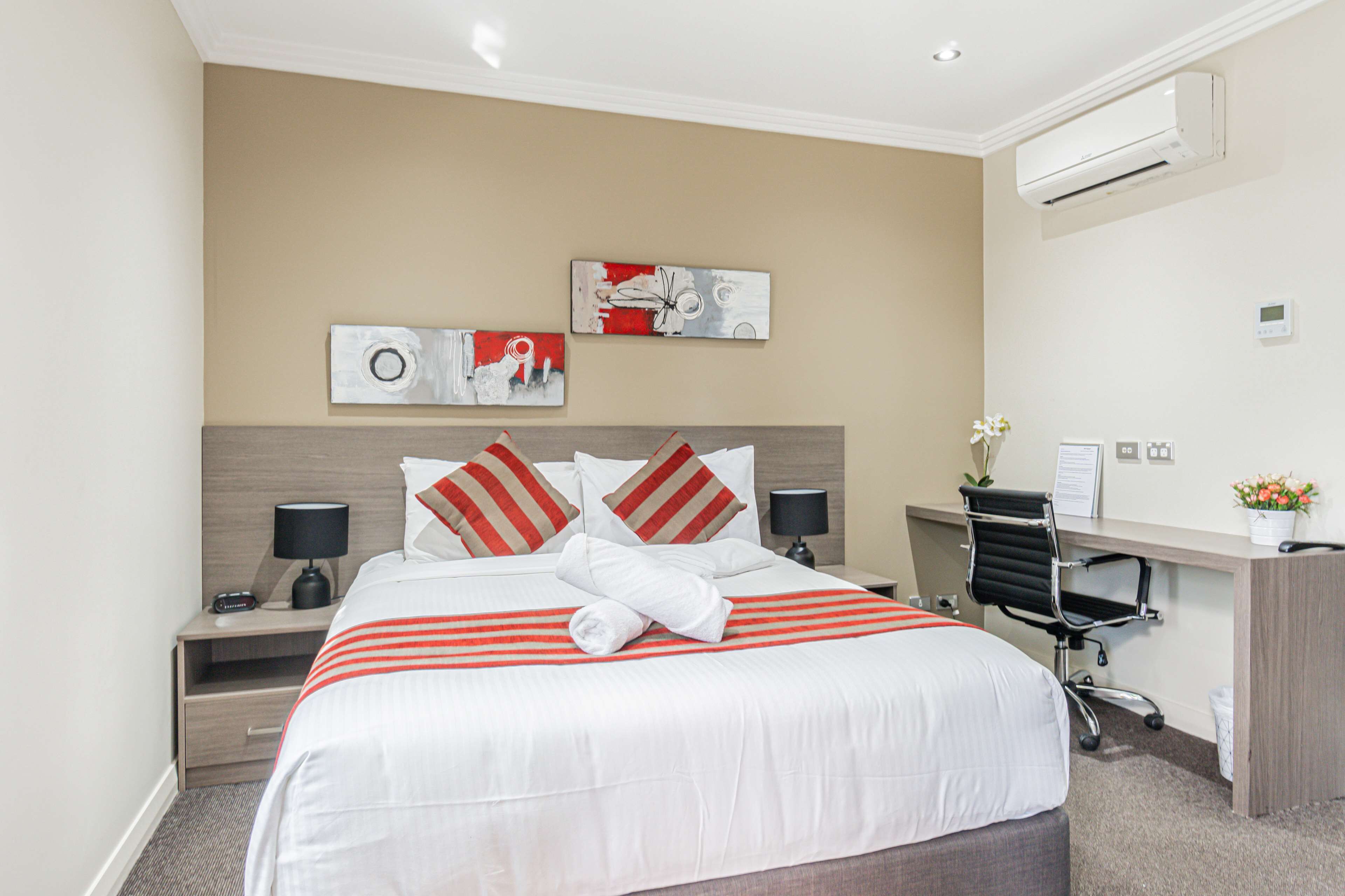 A hotel room with a large bed, two bedside tables with lamps, a desk with a chair, and artwork on the wall.