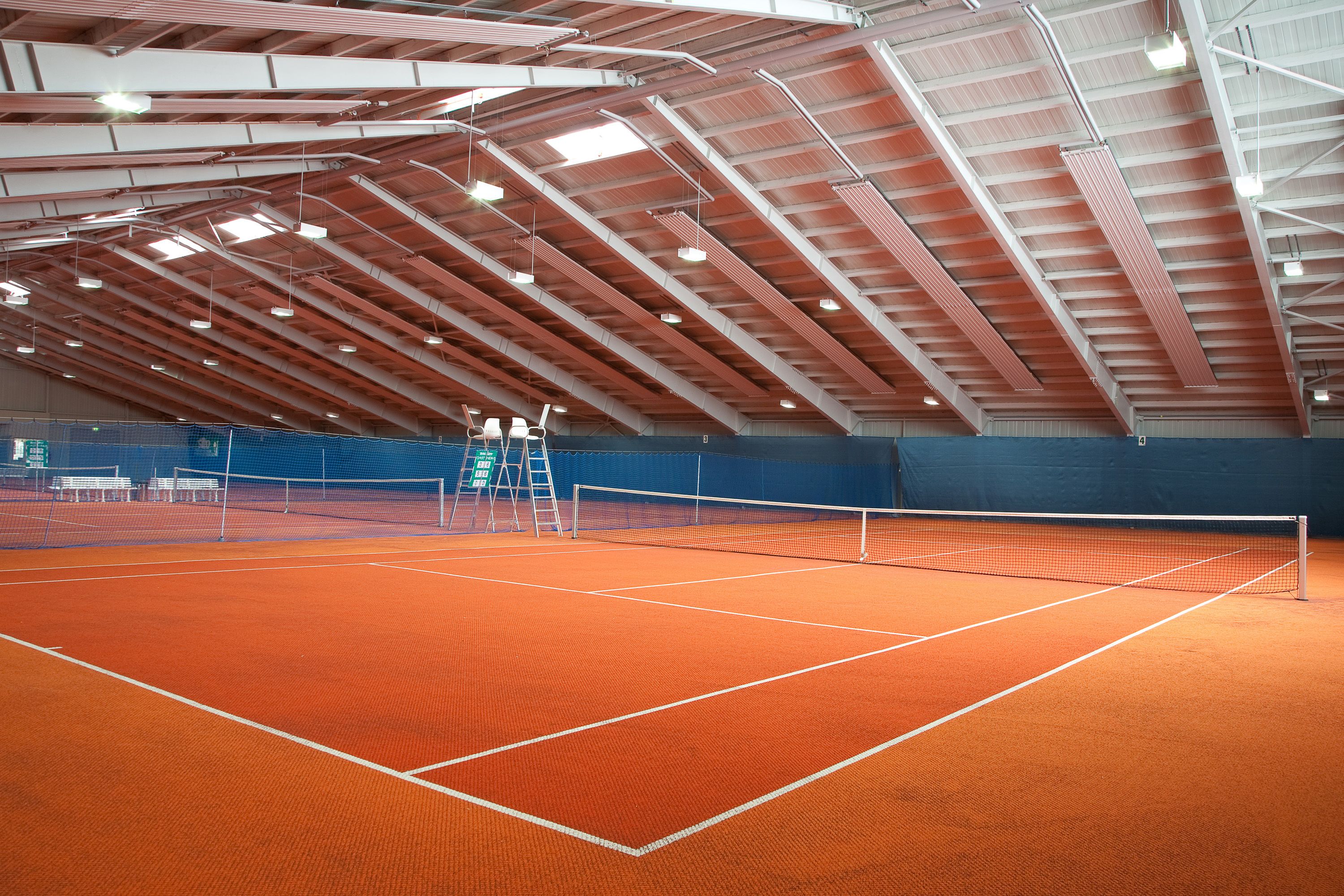 Pista de tenis interior con techo alto y vigas estructurales visibles.