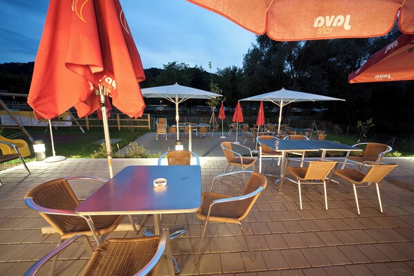 An outdoor patio area with tables and chairs, red umbrellas, and a brick floor. - JUFA Hotel Leibnitz (Leibnitz)