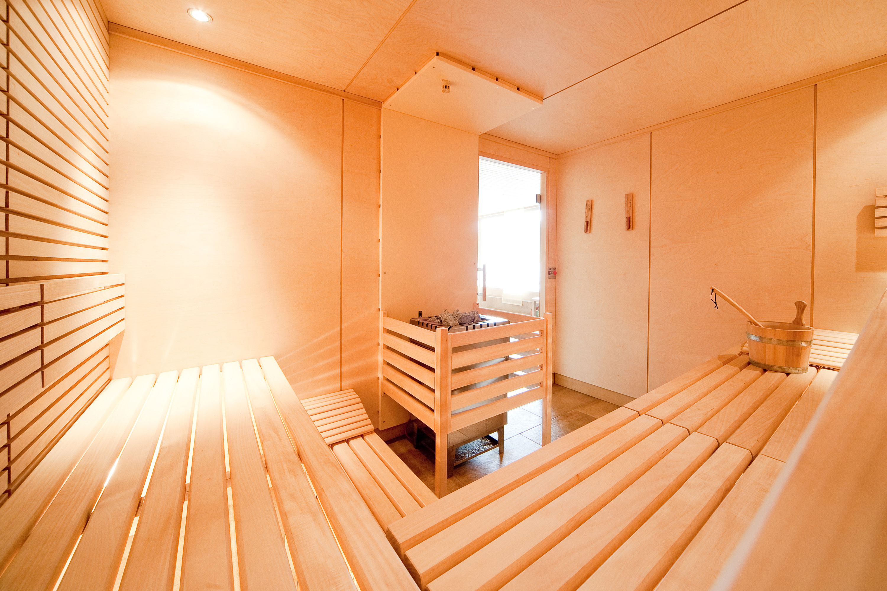 Una sauna de madera con bancos y una pequeña mesa con un cubo.