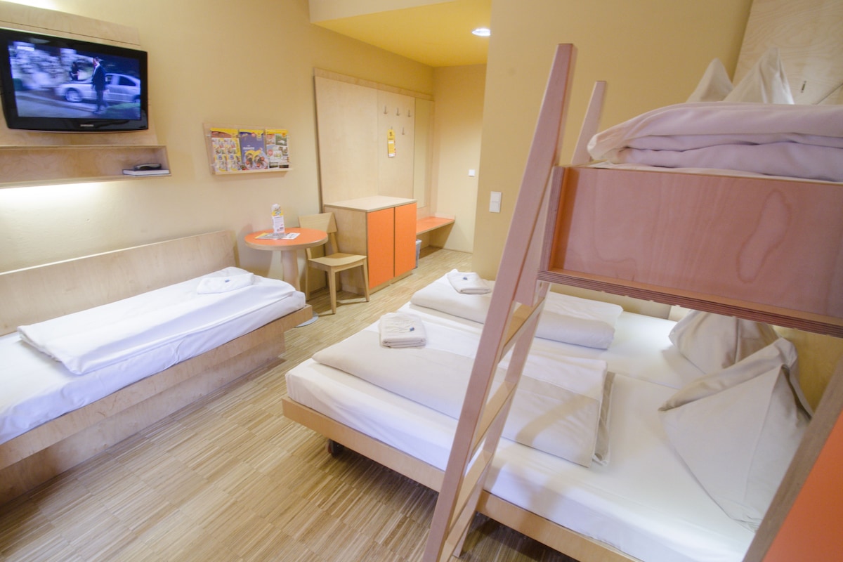 A hotel room with bunk beds, a desk, a chair, and a television on the wall.