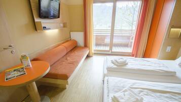 A hotel room with a sofa, a bed, a small table, and a TV mounted on the wall.