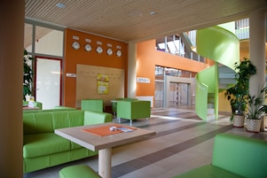 Um hall moderno com assentos verdes, uma mesa de madeira e uma escada em espiral.
