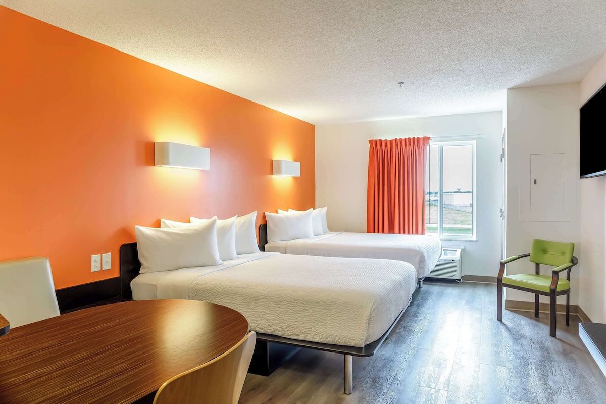 A hotel room with two beds, a dining table, and a TV.