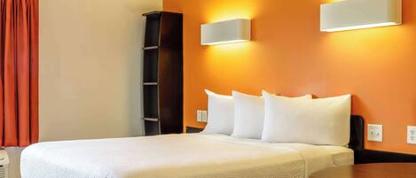 A hotel room with a bed, a nightstand, a wall-mounted light, and a red curtain.